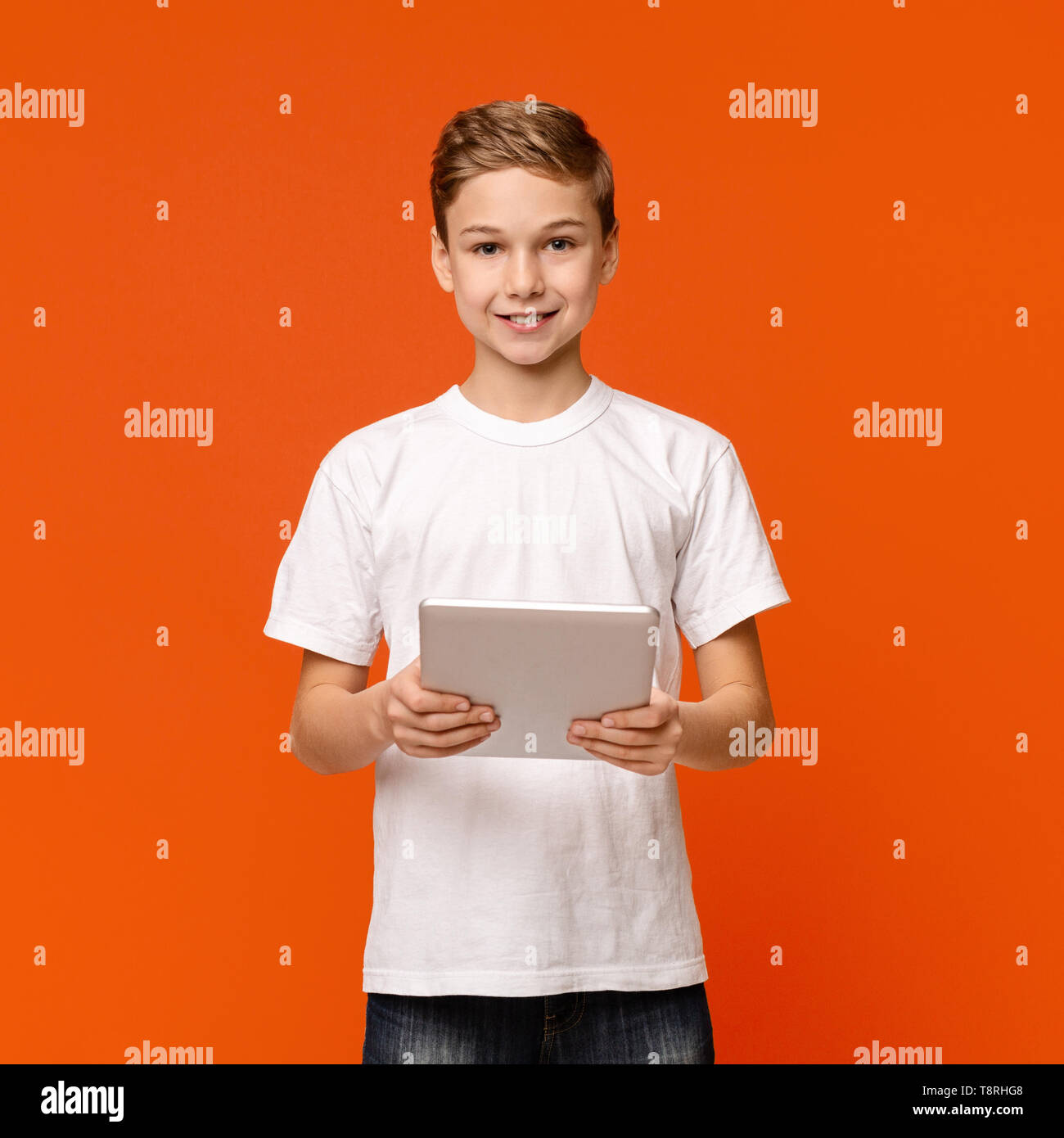 Teen boy using digital tablet on orange studio background Stock Photo