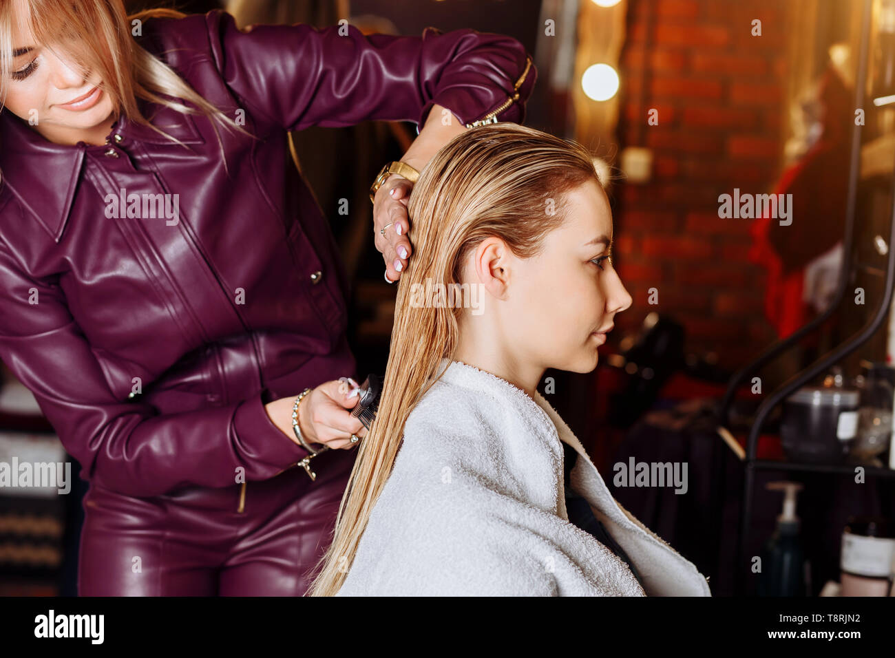 Hairdresser brushing wet hair of beautiful young blond woman in beauty