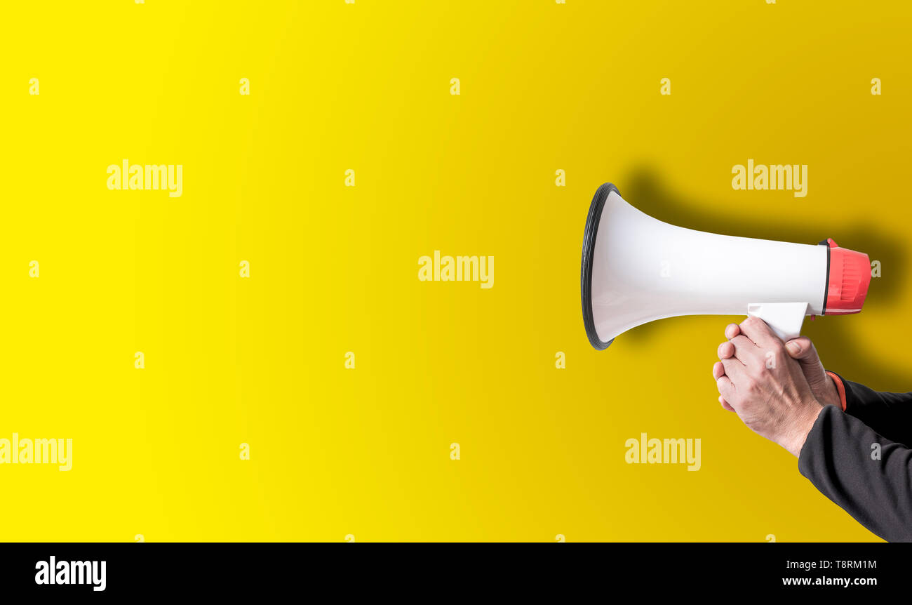 holding megaphone with both hands against yellow background template Stock Photo