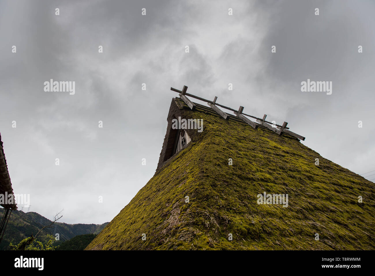 Clouds drift over green straw roof in Japanese mountains Stock Photo