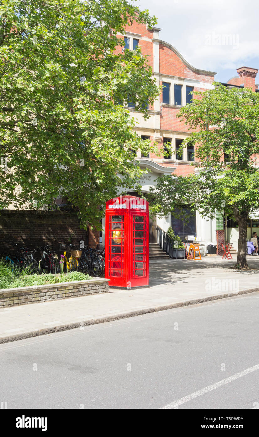 A converted Sir Giles Gilbert Scott K6 phone box, now used to store a defibrillator, in front of the Olympic Cinema, Church, Barnes, London, SW13, UK Stock Photo