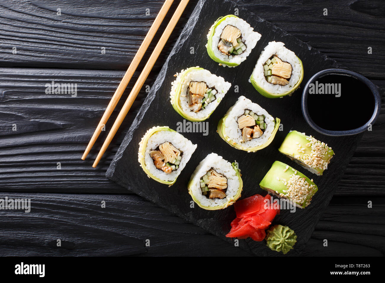 Japanese rolls wrapped in avocado with omelet, sesame and cucumber closeup on a plate on the table. Horizontal top view from above Stock Photo