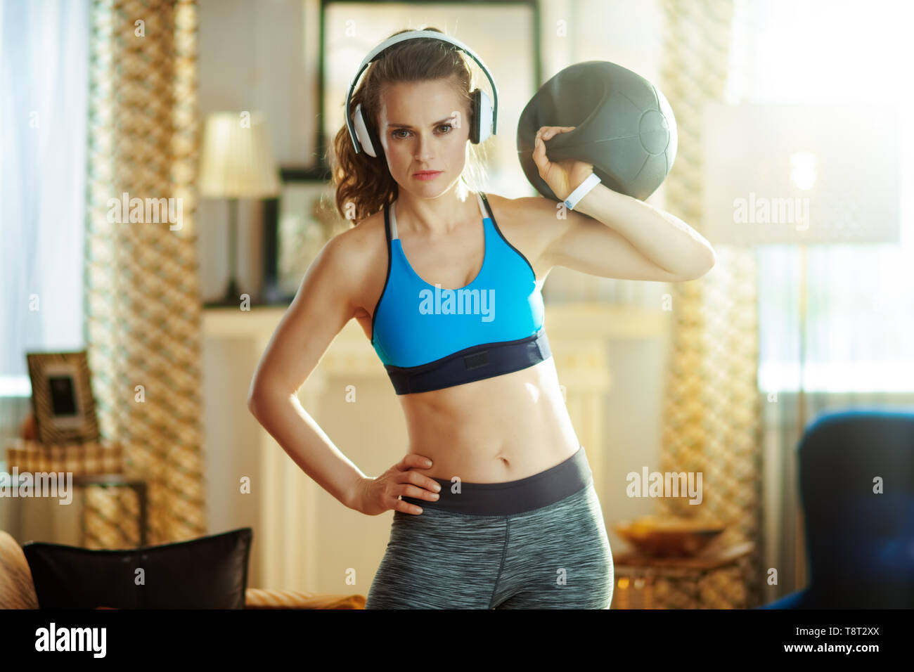 healthy woman in headphones in fitness clothes with functional training gear at modern home. Stock Photo