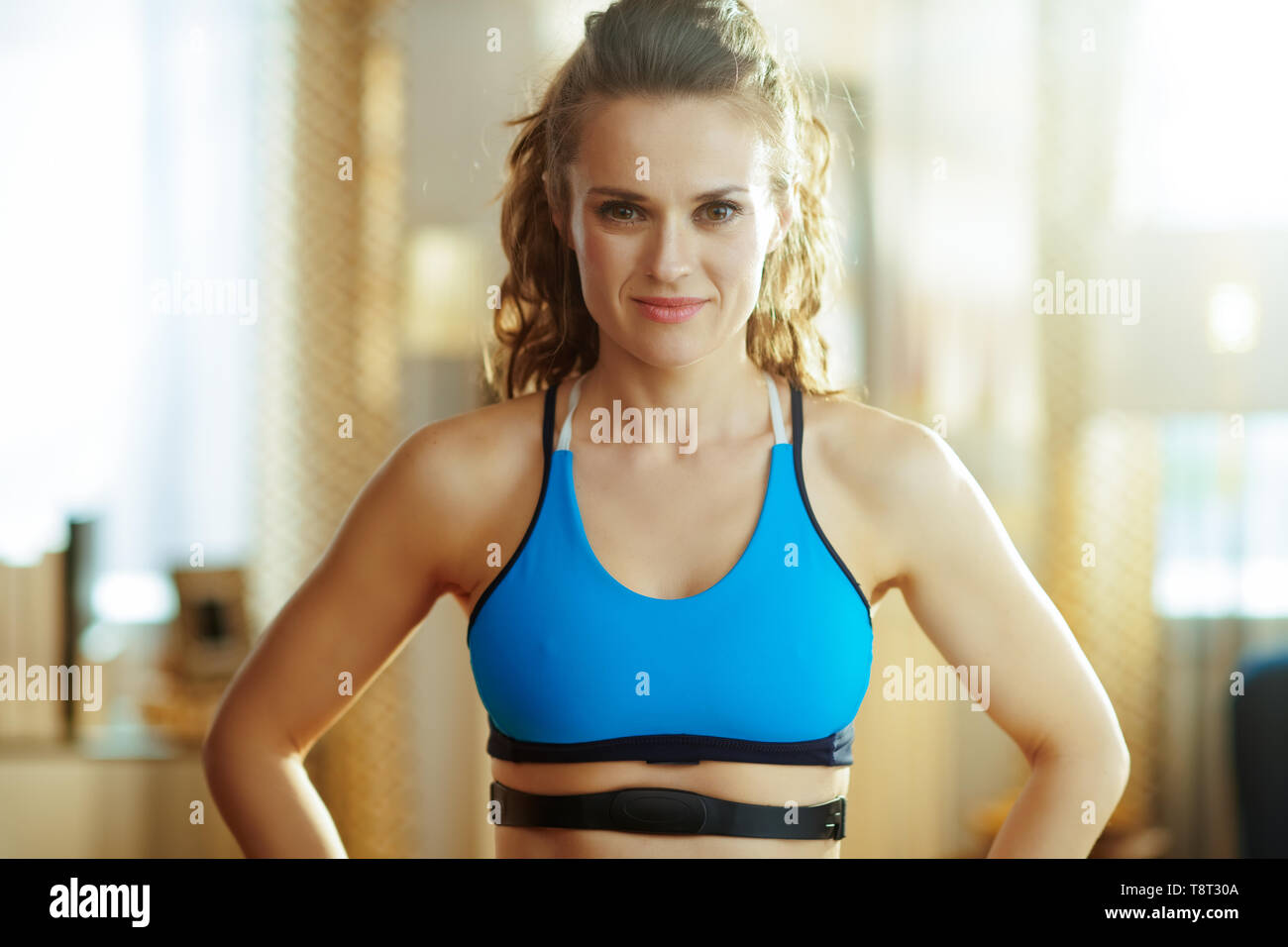 Portrait of healthy sports woman in fitness clothes with heart rate monitor in the modern living room. Stock Photo