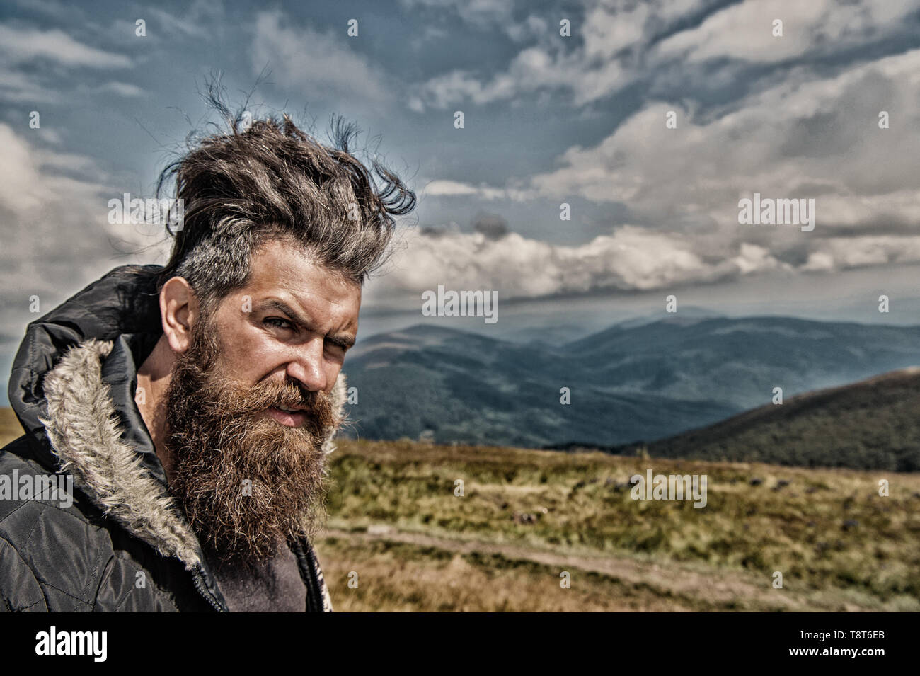 Man hipster with long beard hair, mustache on bearded face with stylish haircut on mountain landscape. Wanderlust, travelling, vacation concept Stock Photo