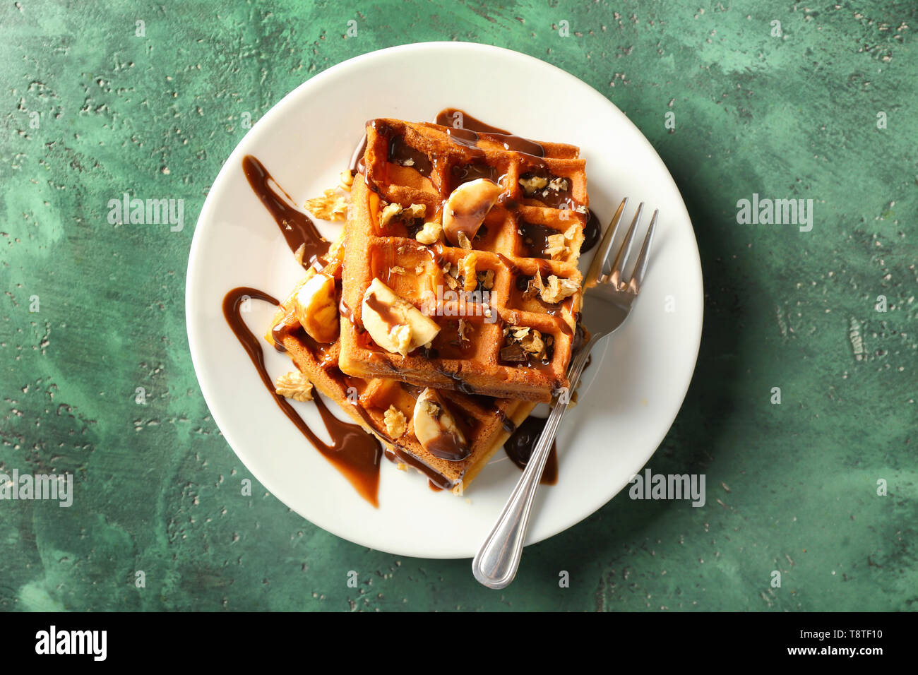 Delicious waffles with banana slices and chocolate sauce on color table ...