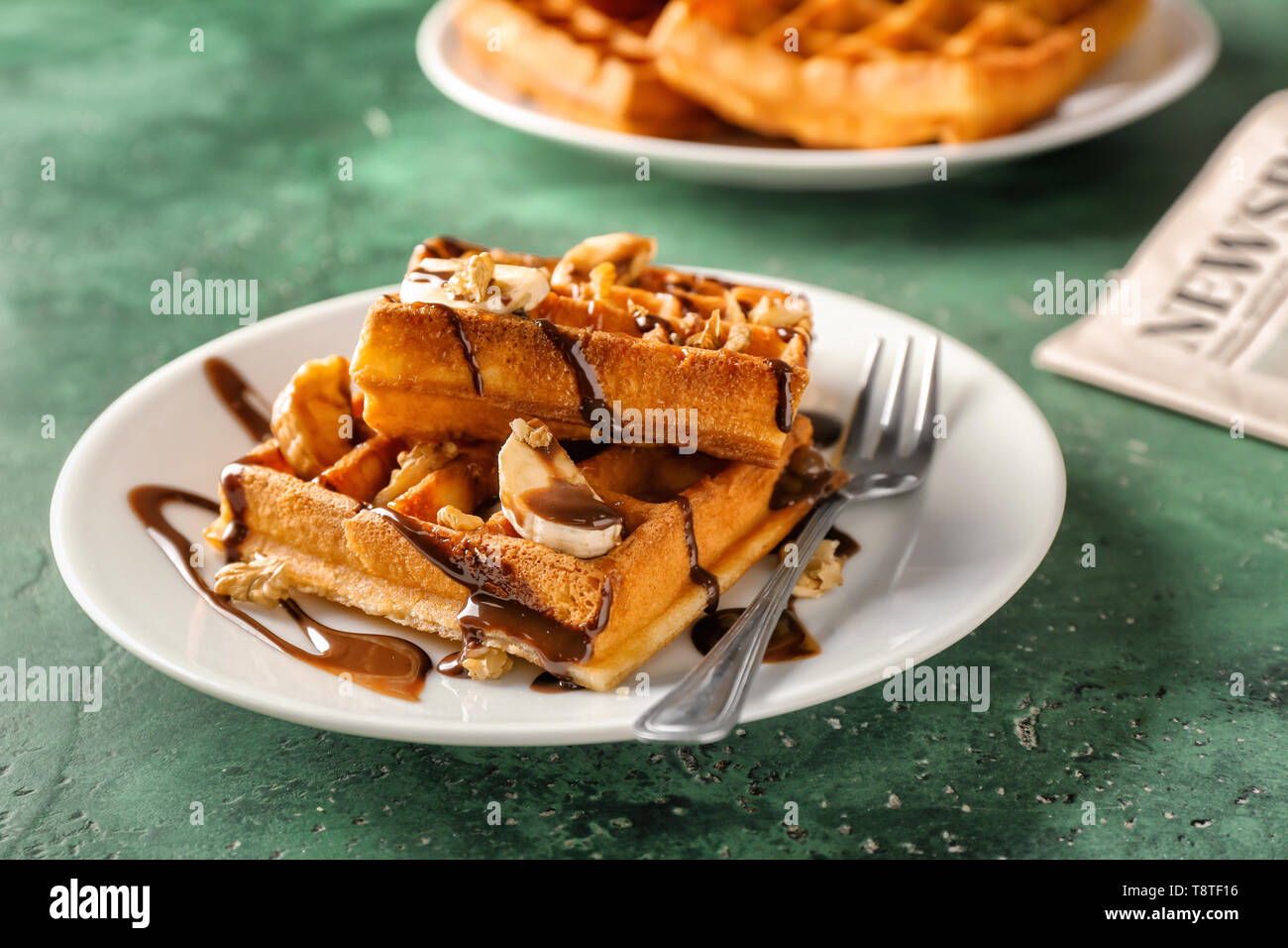 Delicious waffles with banana slices and chocolate sauce on color table ...