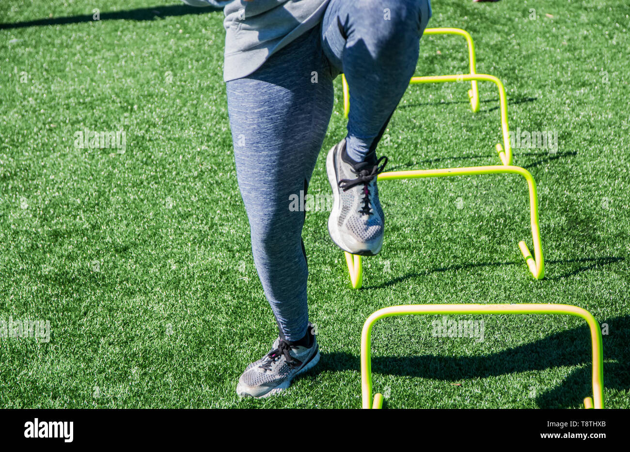 A high school athlete is at track and field practice warming up by running over the side of yellow mini hurdles. Stock Photo