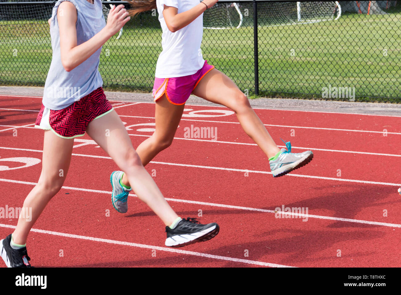 Two high school track and field athletes perform straight leg bounding on a red track at practice outside Stock Photo