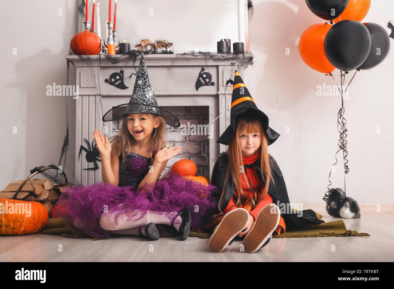 Cute little girls in Halloween costumes near decorated fireplace Stock