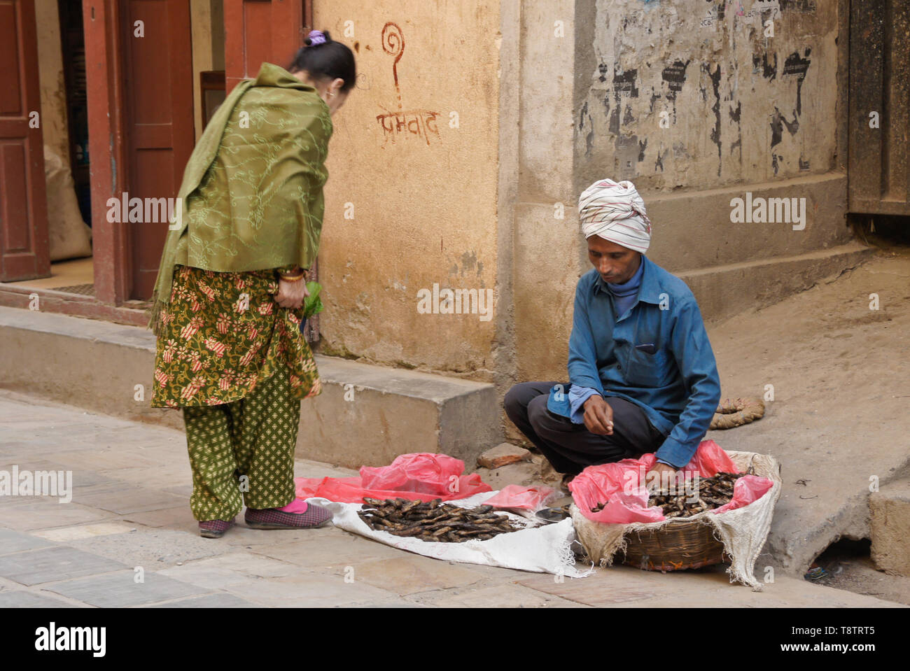 Street vendor selling dried fish to woman in traditional dress, Kathmandu, Nepal Stock Photo