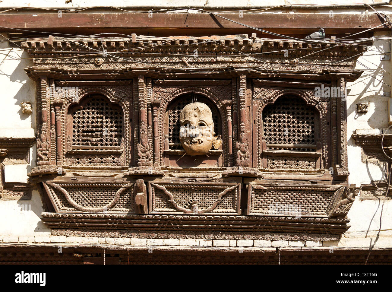 Window with carved wood screen and mask on old building near Durbar Square, Kathmandu, Nepal Stock Photo