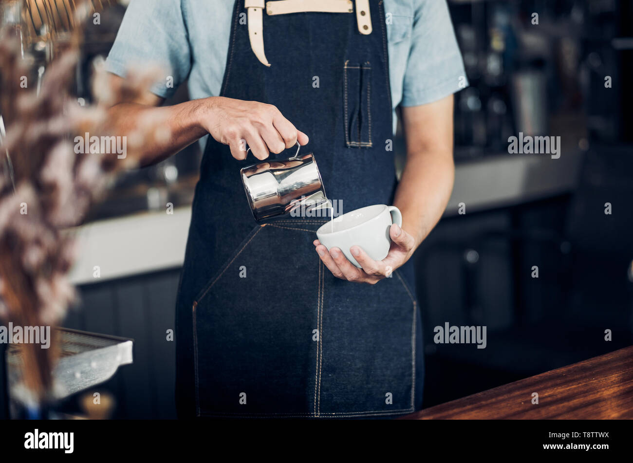 Man barista pour milk into hot coffee cup at counter bar in front of machine in cafe restaurant,Food business owner concept. Stock Photo