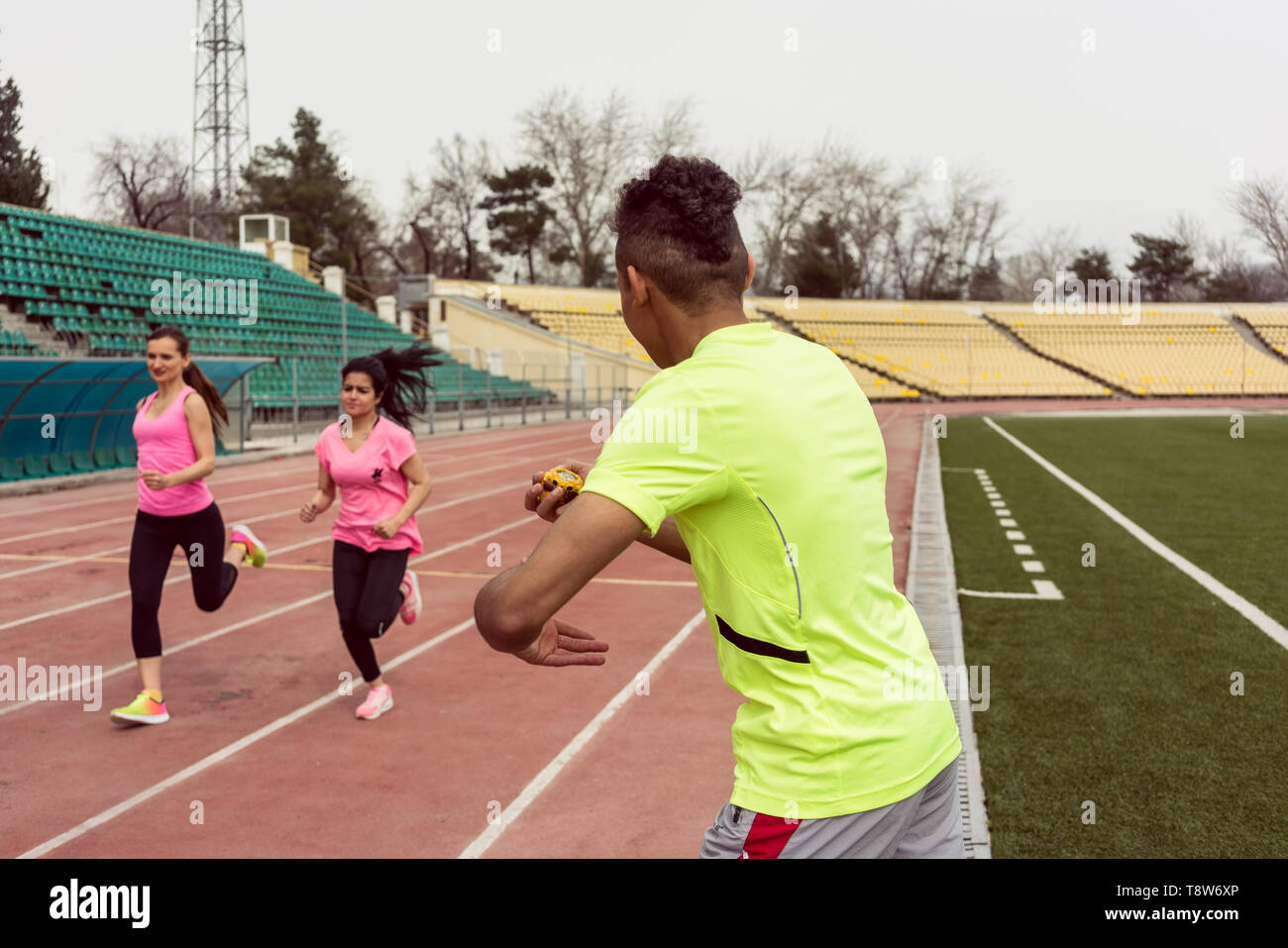 Rear view of a man holding stop watch while two female athletic running on ground Stock Photo