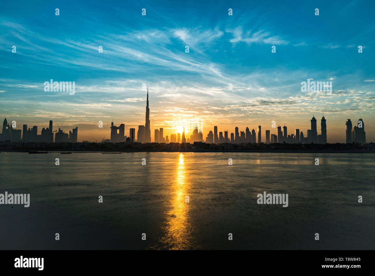 Sunrise in Dubai, dawn, morning or dusk over modern city. Sun over buildings or skyscrapers. Solar path on the sea. Stock Photo