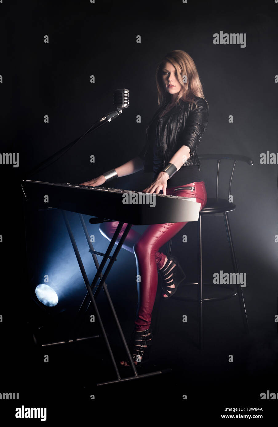 Blonde girl musician pianist plays perform on white digital piano, sits on chair, sings into retro microphone. Woman teacher shows how to play music Stock Photo