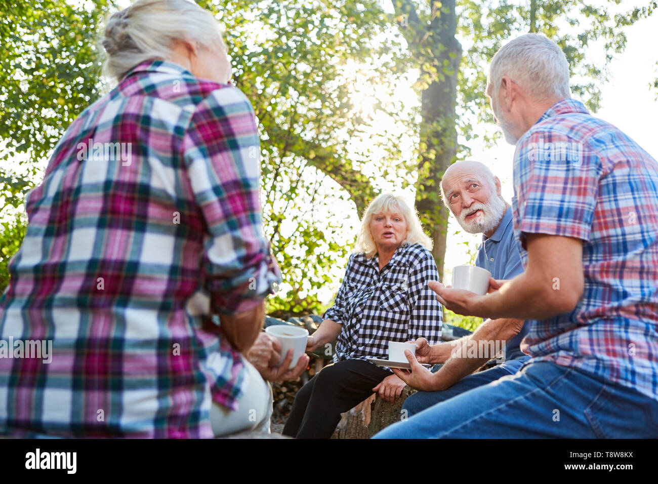 Seniors sit relaxed with a cup of coffee in the garden and talk Stock Photo