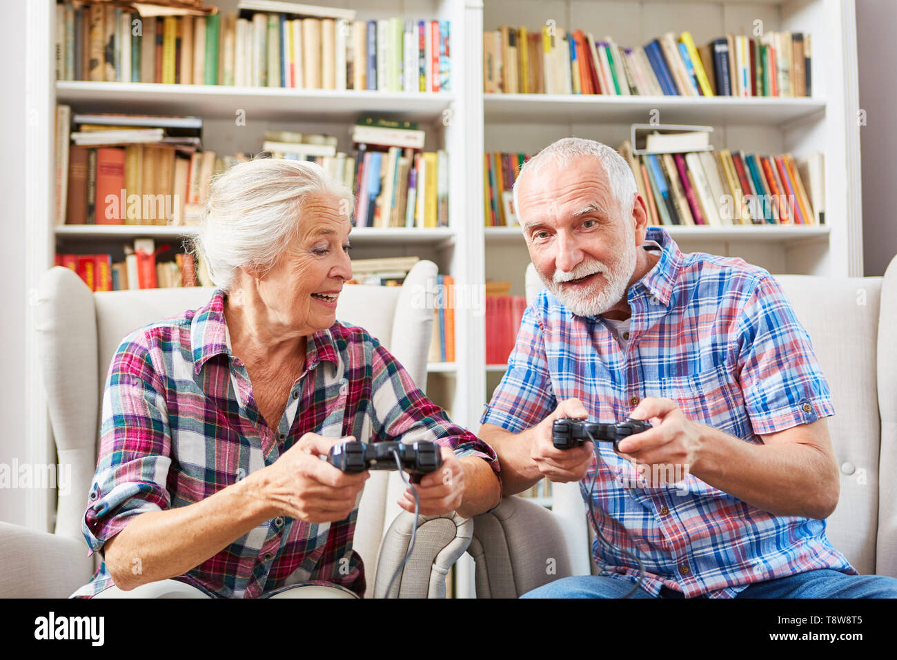 Senior couple plays video game with console against each other in the living room Stock Photo