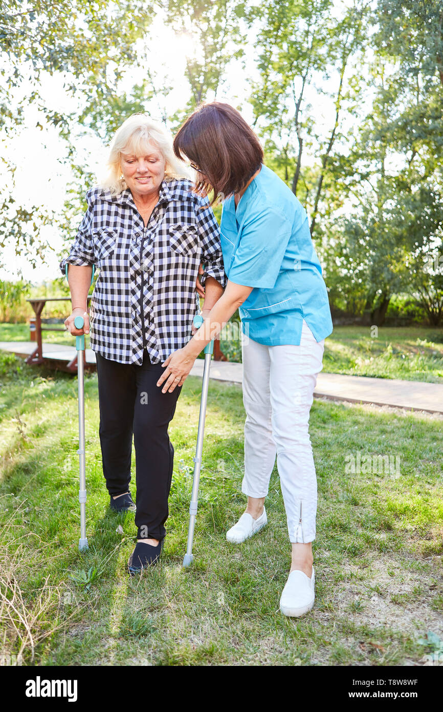 Nursing woman helps senior woman with crutches while walking learning