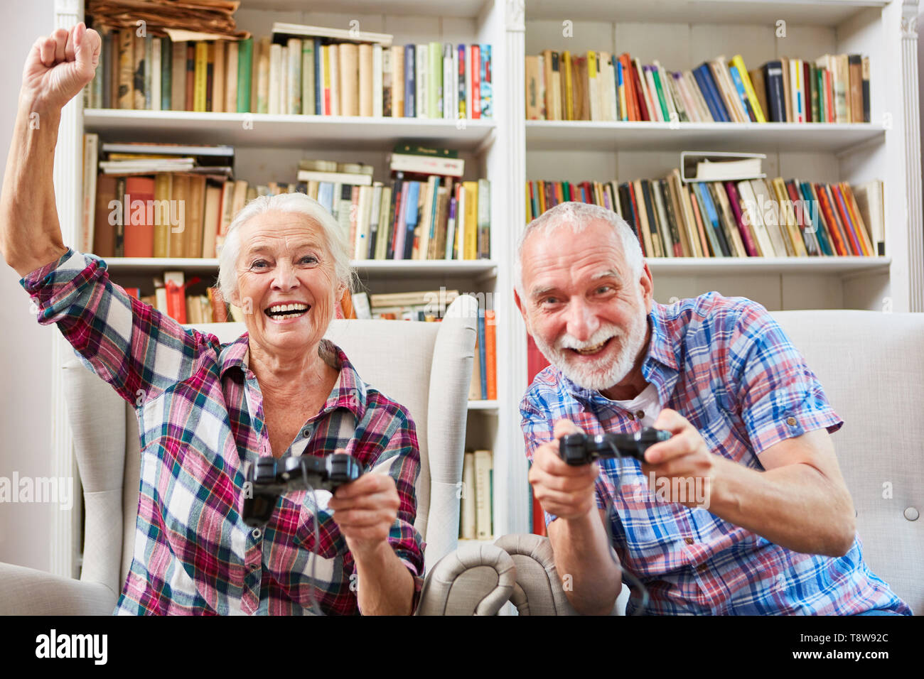 Laughing couple of seniors playing video game against one with console in the living room Stock Photo