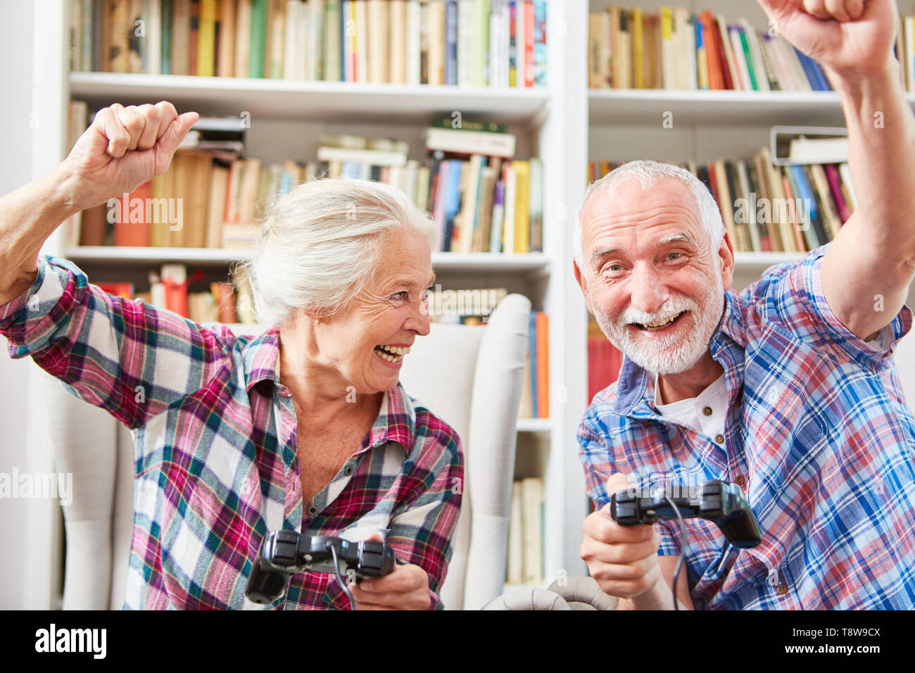 Cheering senior couple plays video game with console indoors in the living room Stock Photo