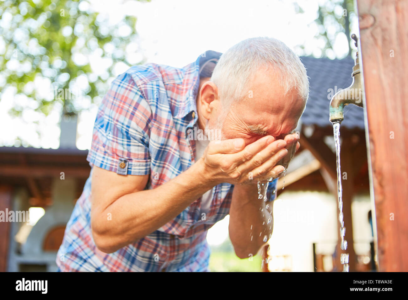 Senior man washes his face at a water tap on a farm Stock Photo