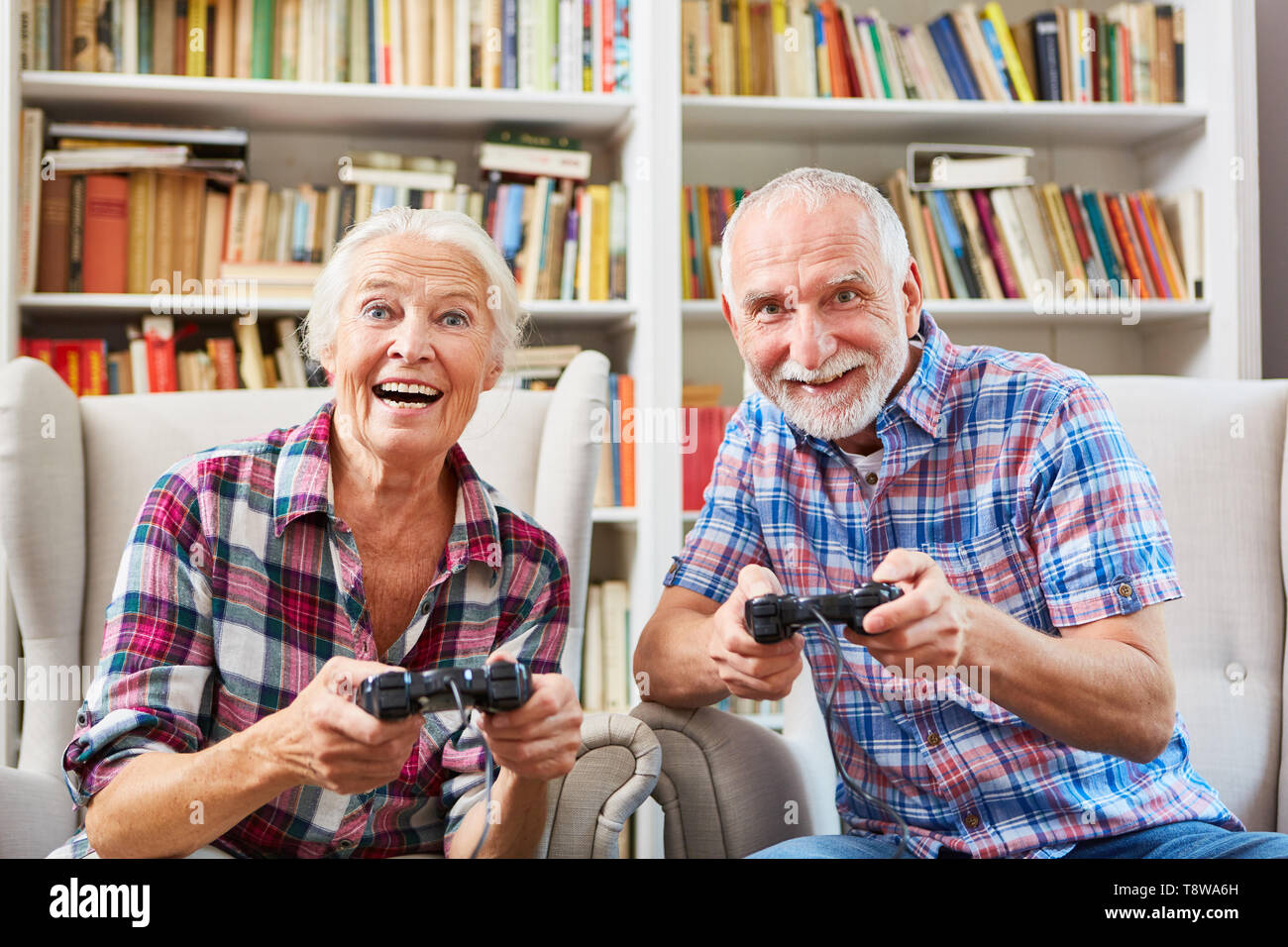 Happy couple of seniors enthusiastically plays video game with console at home Stock Photo