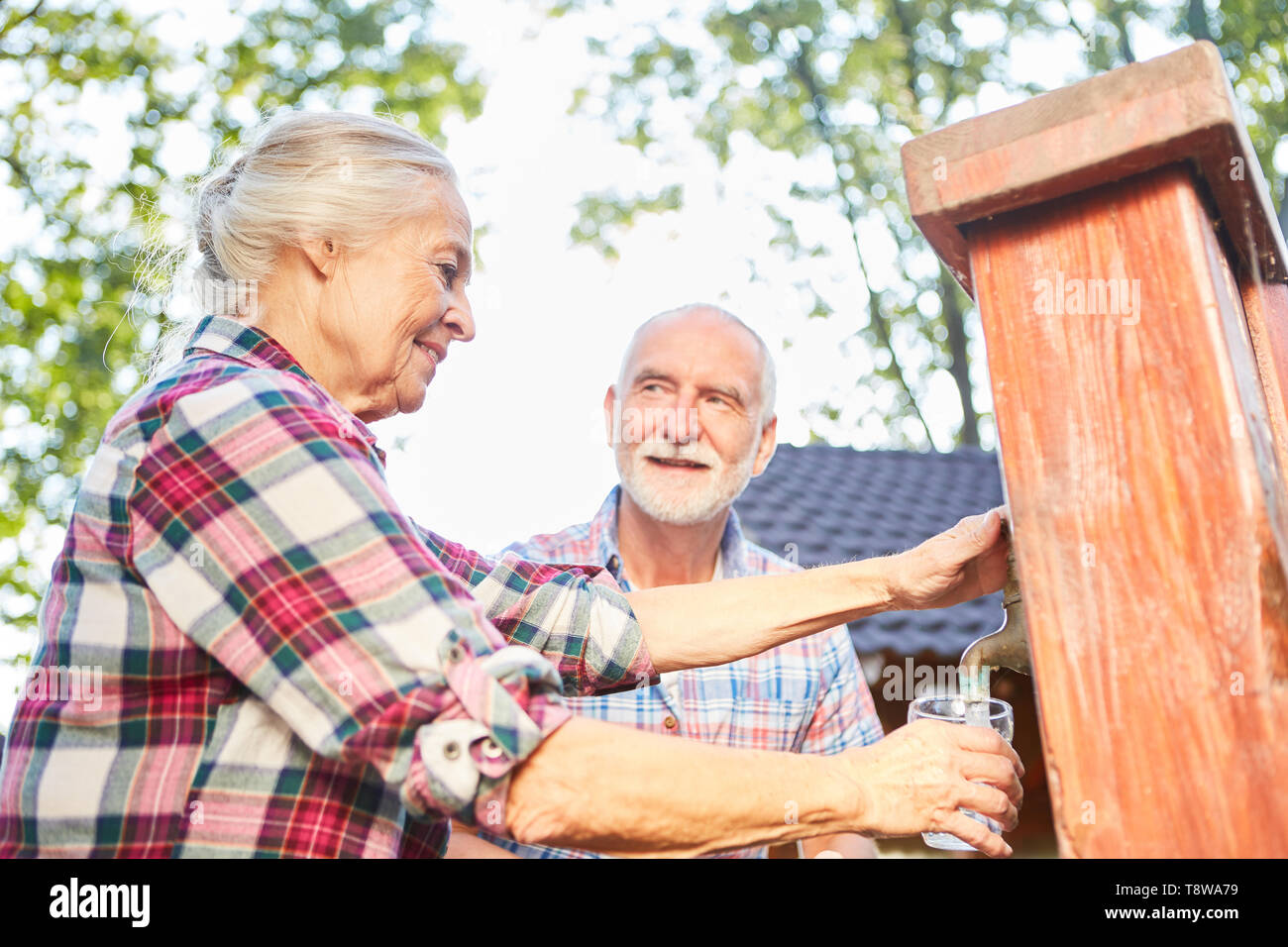 Senior couple fills water into a glass at a fountain on a farm Stock Photo