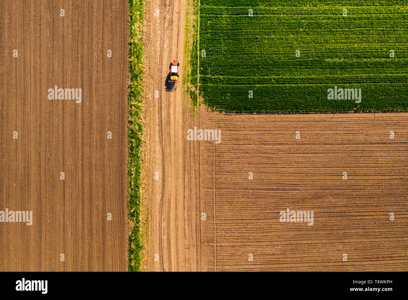 Aerial view of tractor with attached crop sprayer on countryside dirt road heading toward the field, top down view from drone pov Stock Photo