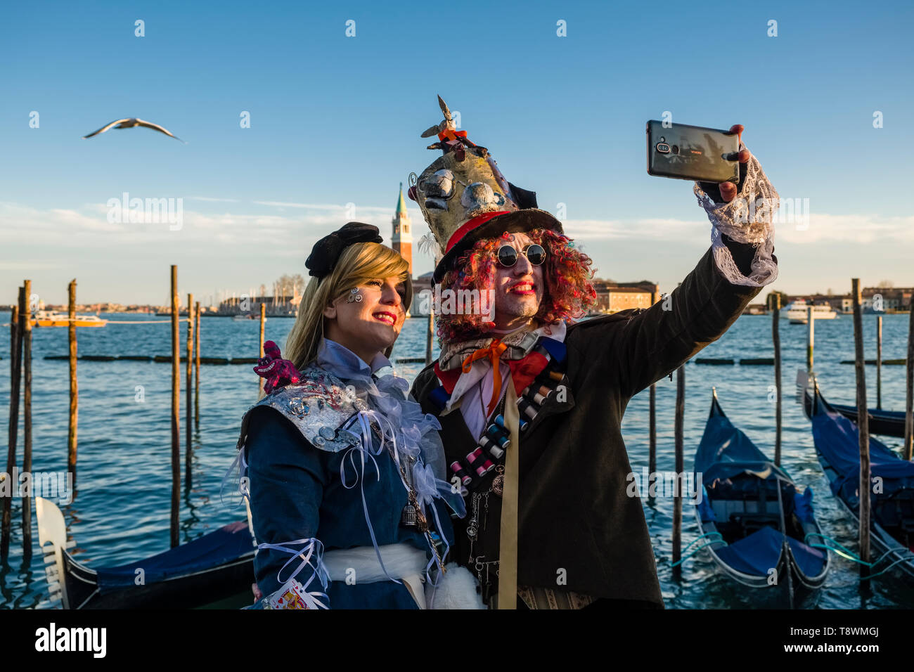 Two masked and costumed people are taking a selfie with a mobile phone at the Grand Canal, Canal Grande, celebrating the Venetian Carnival Stock Photo