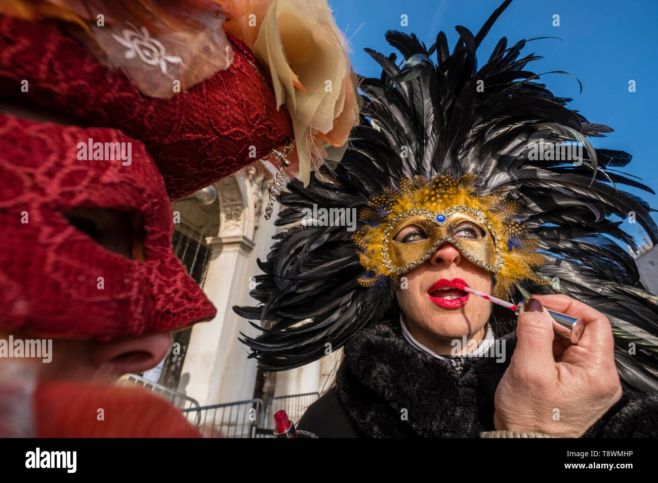 Two masked and costumed people are doing their make up at San Marco Square, Piazza San Marco, celebrating the Venetian Carnival Stock Photo