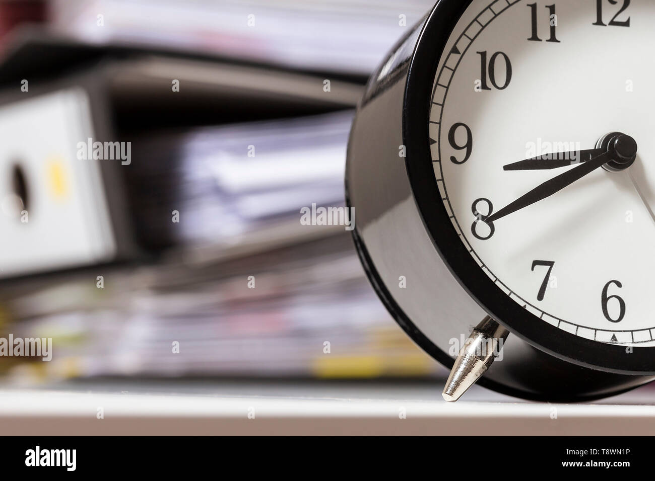 Alarm clock in an office next to a pile of files Stock Photo