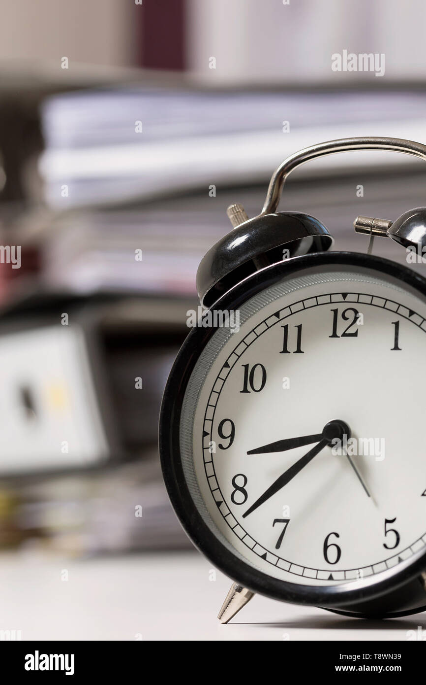 Alarm clock in an office next to a pile of files Stock Photo