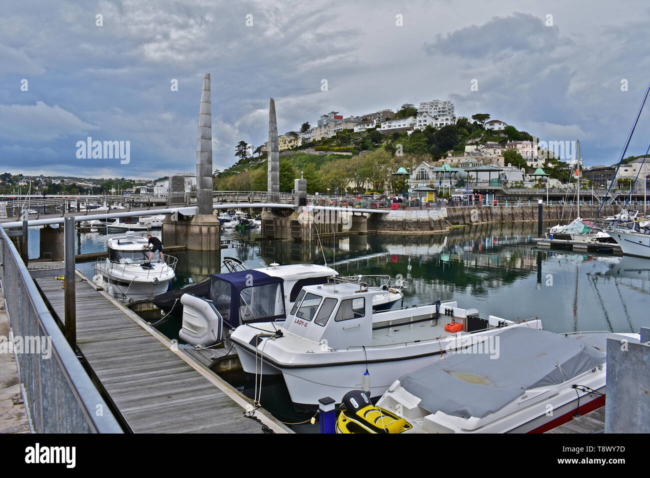 A view across the inner harbour/ marina at Torquay with yachts at moorings. Calm still waters with reflections of boats and buildings on the hillside. Stock Photo