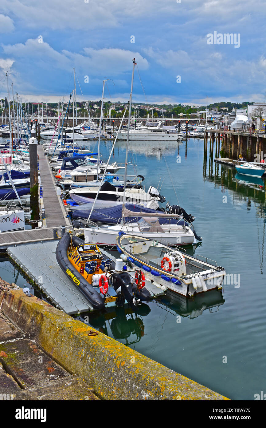 A view across the inner harbour/ marina at Torquay with yachts at moorings. Calm still waters with reflections of boats and buildings on the hillside. Stock Photo