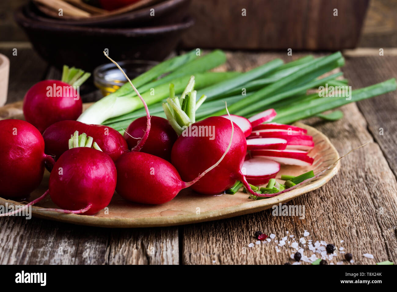Fresh springtime radishes, green onion and garlic on rustic wooden background, plant based food cooking ingredients, close up, selective focus Stock Photo