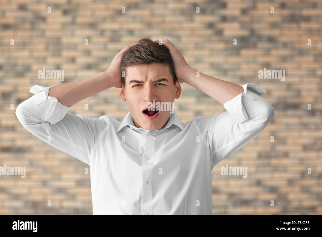 Portrait of handsome stressed young man against brick wall Stock Photo ...