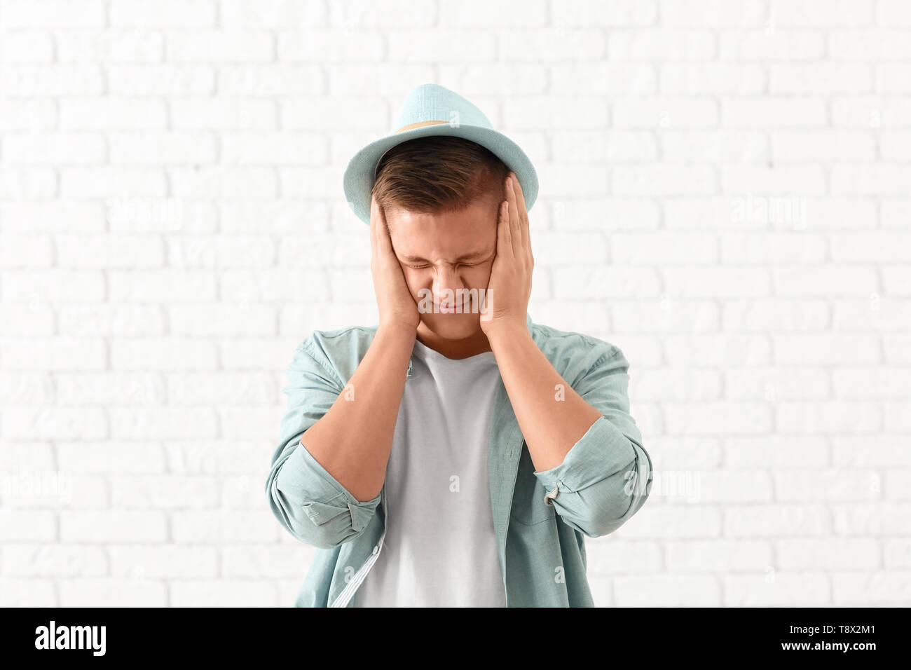Portrait of handsome stressed young man against white brick wall Stock ...