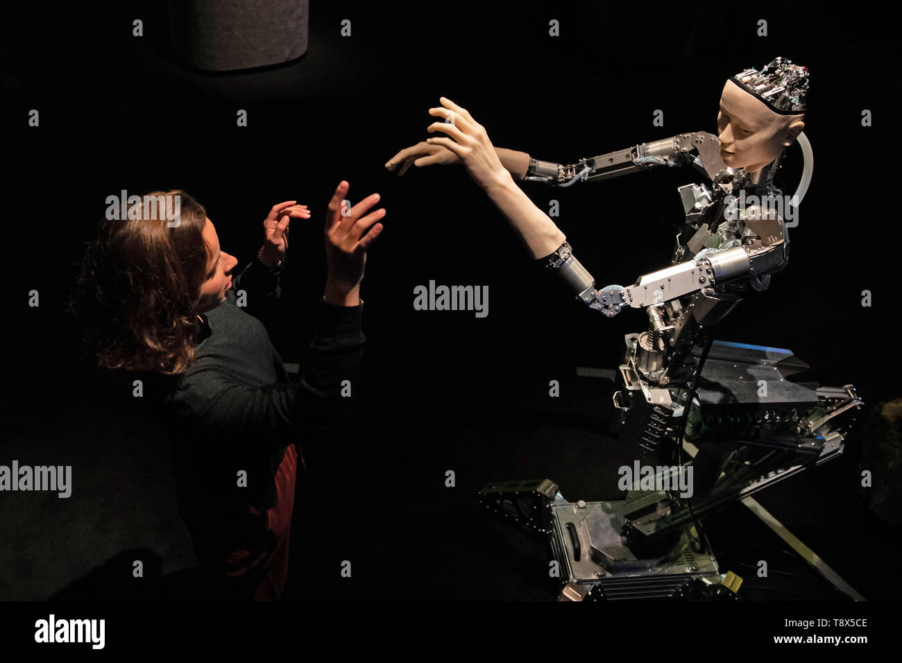 A women interacts with 'Alter', a machine body with a human like face and hands who learns through interplaying with the surrounding world. Alter was created by roboticist Hiroshi Ishiguro and is on display at the 'AI: More Than Human' exhibition at the Barbican Centre in London. The major new exhibition explores the relationship between humans and artificial intelligence. Stock Photo