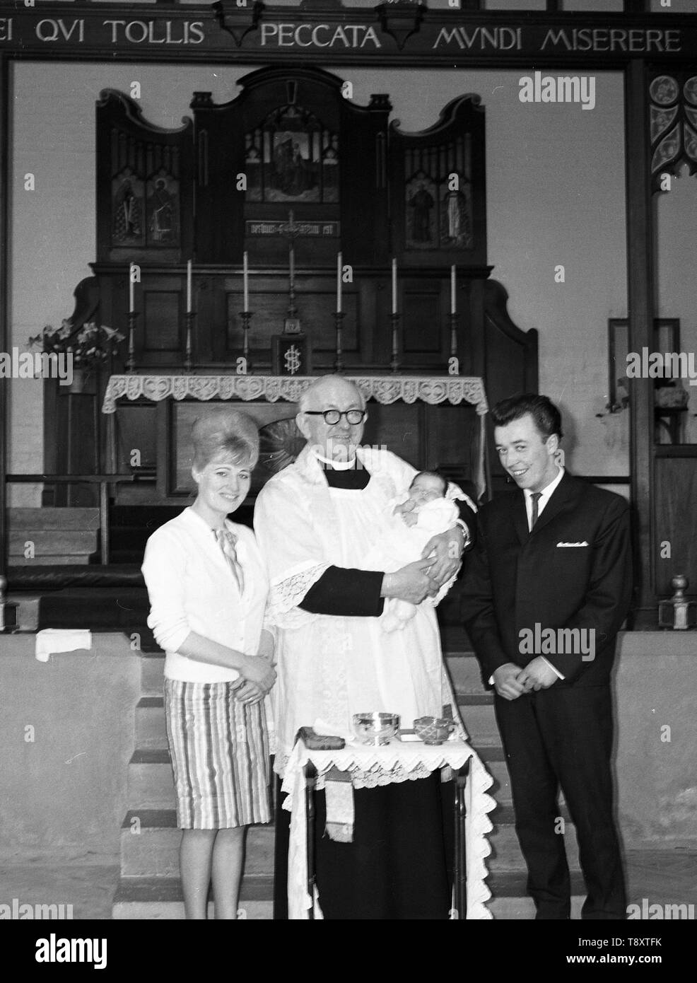 A Baby Christening in the UK c1962  Mum, Dad with baby and Vicar inside the church  Photo by Tony Henshaw Stock Photo