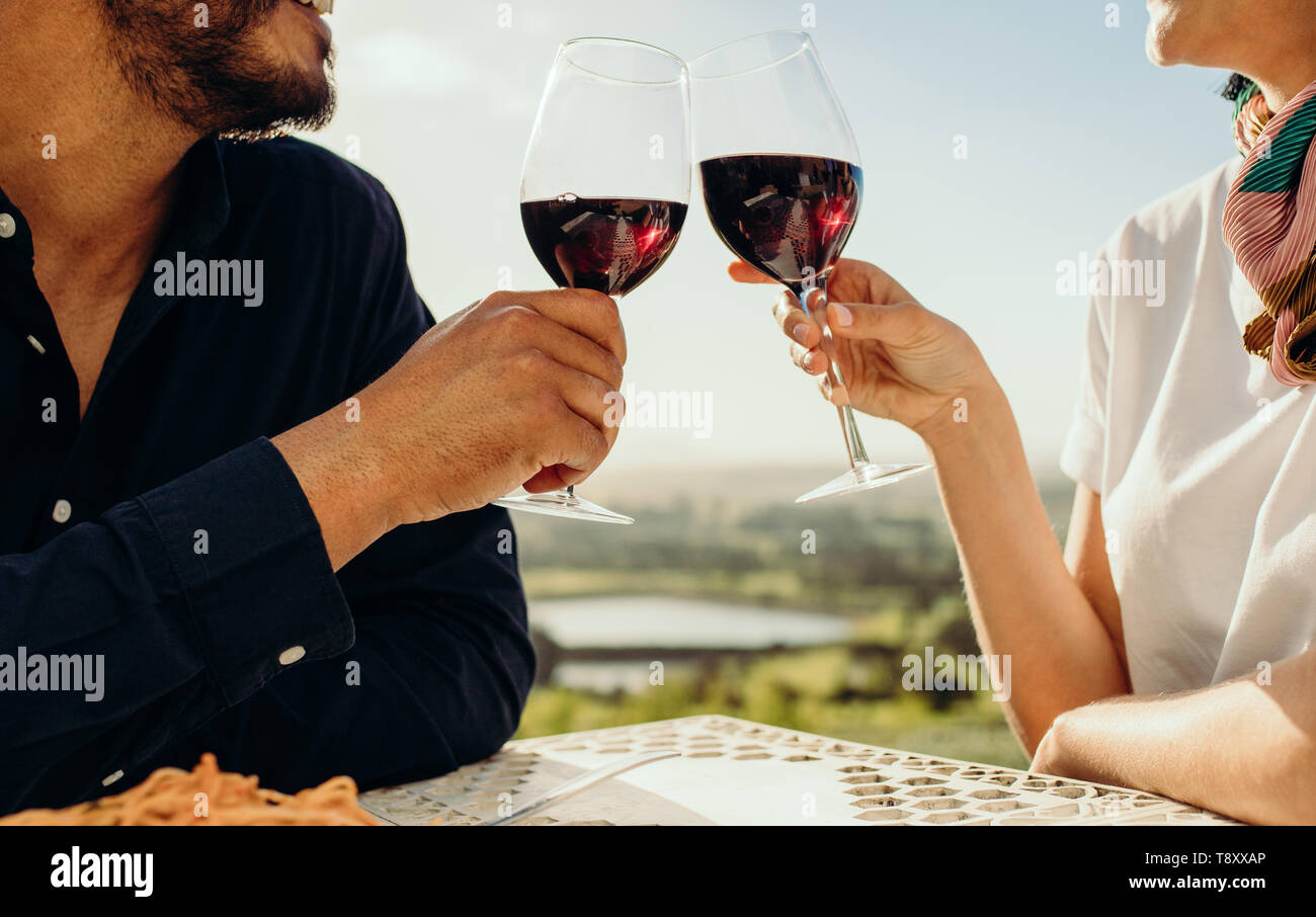 Cropped shot of a couple sitting together with a glass of wine. Side view of a couple on a date talking to each other toasting glasses of red wine. Stock Photo