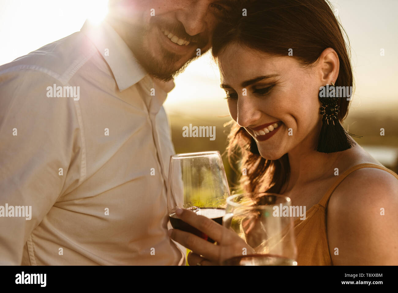 Cropped shot of a happy couple laughing together holding glass of red wine. Side view close up of a smiling couple on a romantic wine date. Stock Photo