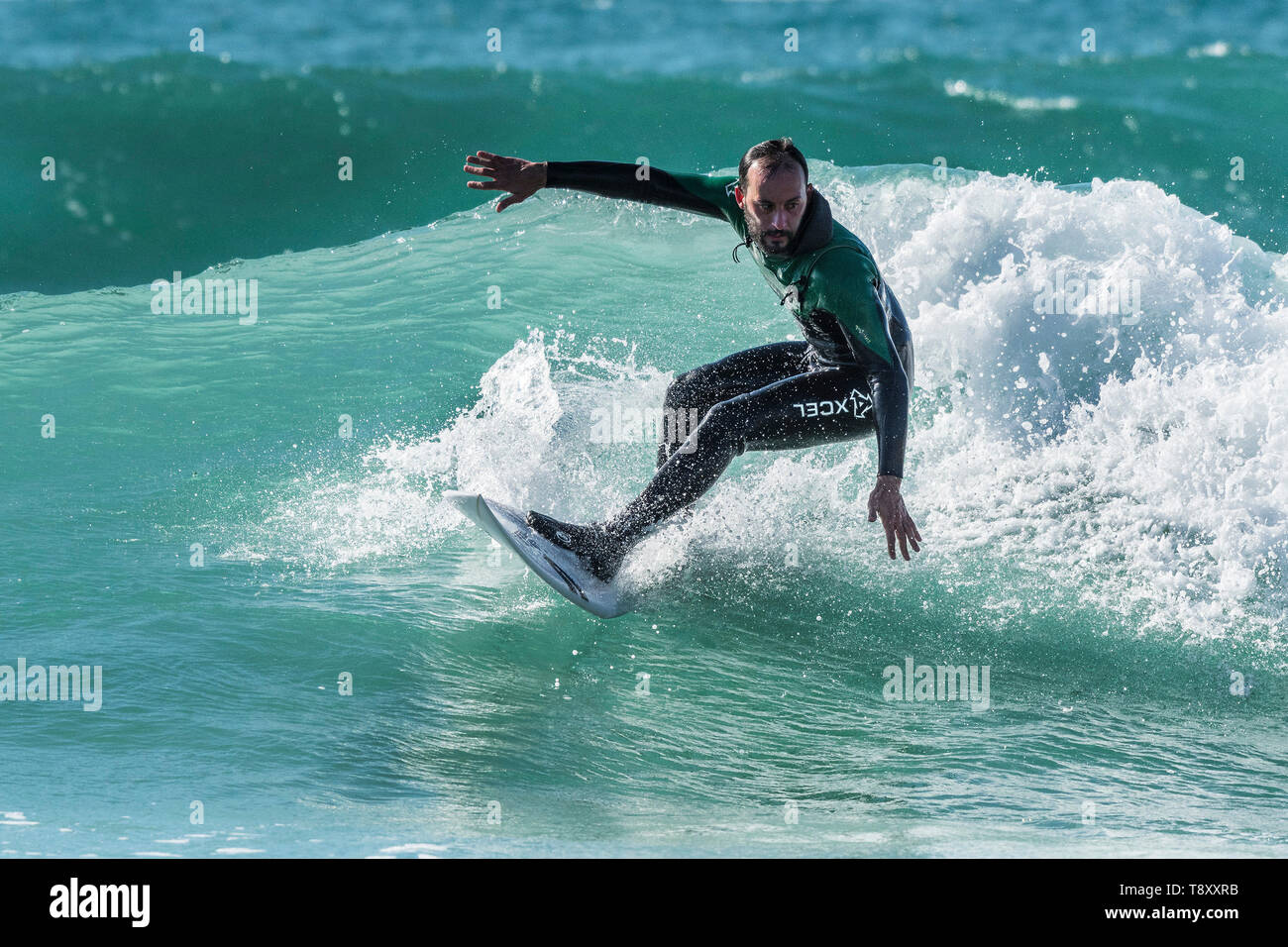 Spectacular surfing action as a surfer wearing an Xcel wetsuit rides a wave in a jade coloured sea at Fistral in Newquay in Cornwall. Stock Photo