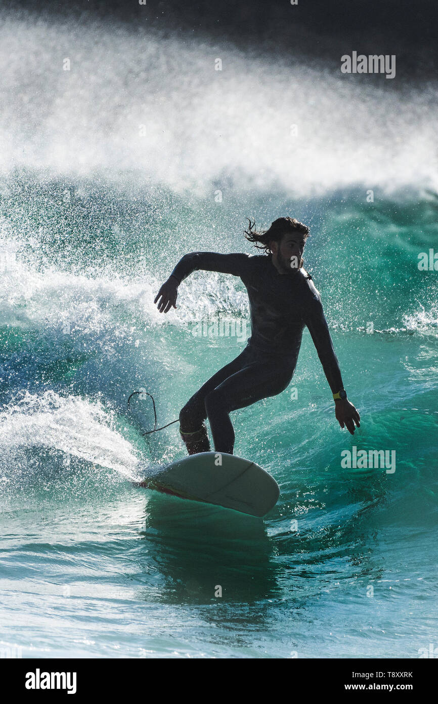 Surfing action as a surfer is silhouetted against the sunlight as rides a wave in a jade coloured sea at Fistral in Newquay in Cornwall. Stock Photo