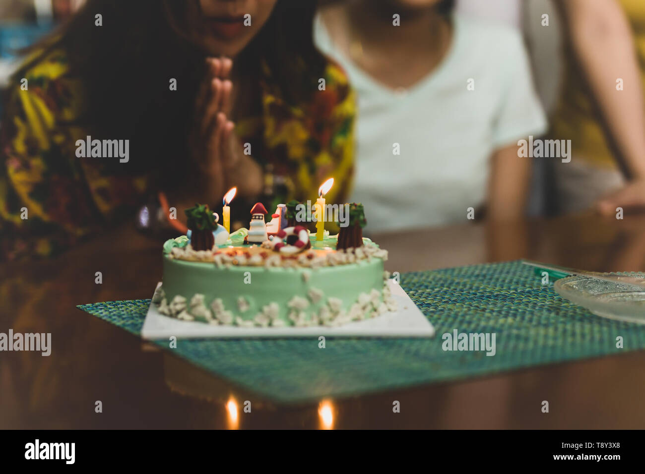 Shot in low light woman blowing on candles on birthday cake with friends. Stock Photo