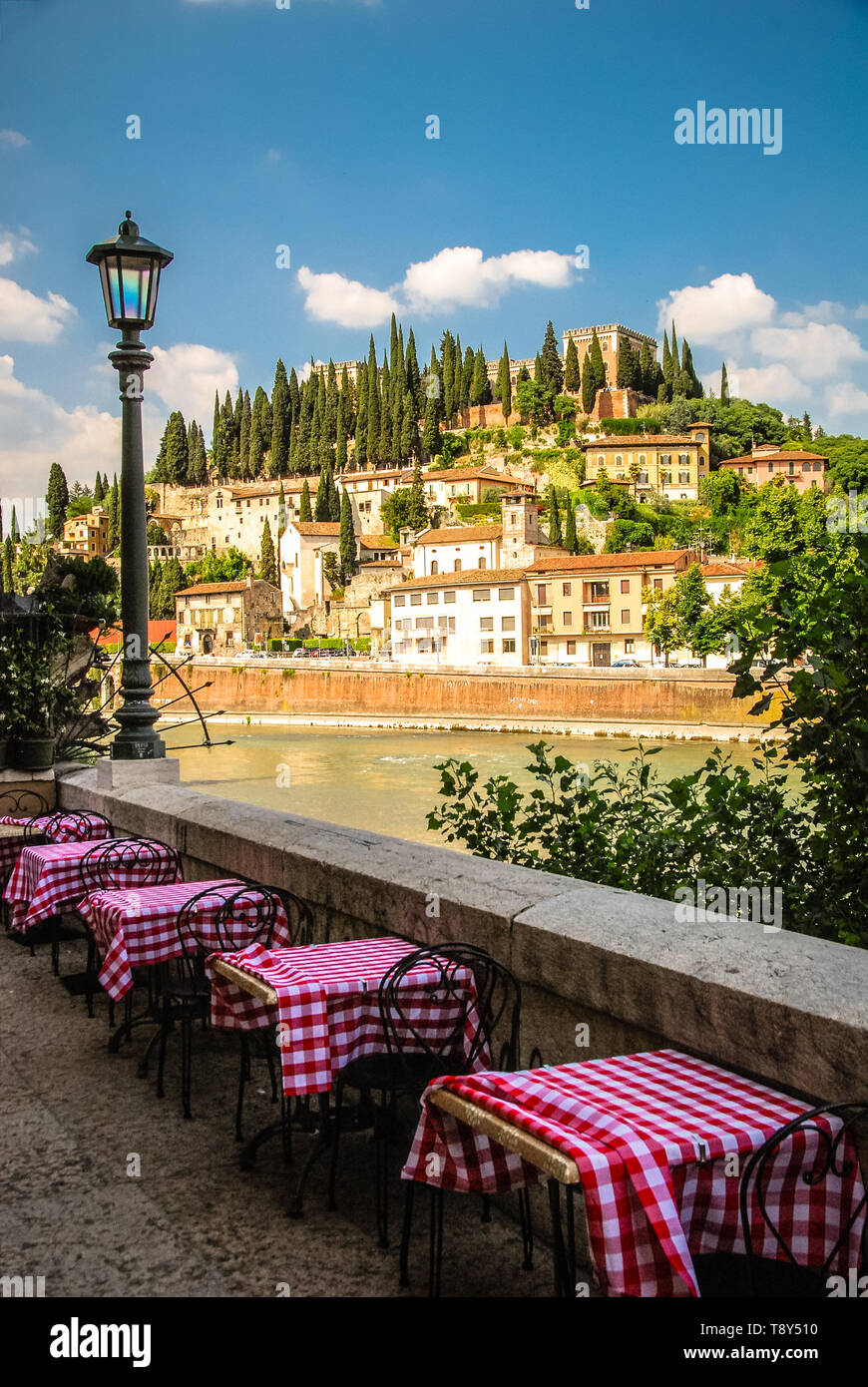 Dining Tables setup along the Adige River in Verona, Italy complete with typical Italian red and white checked tablecloths. Stock Photo