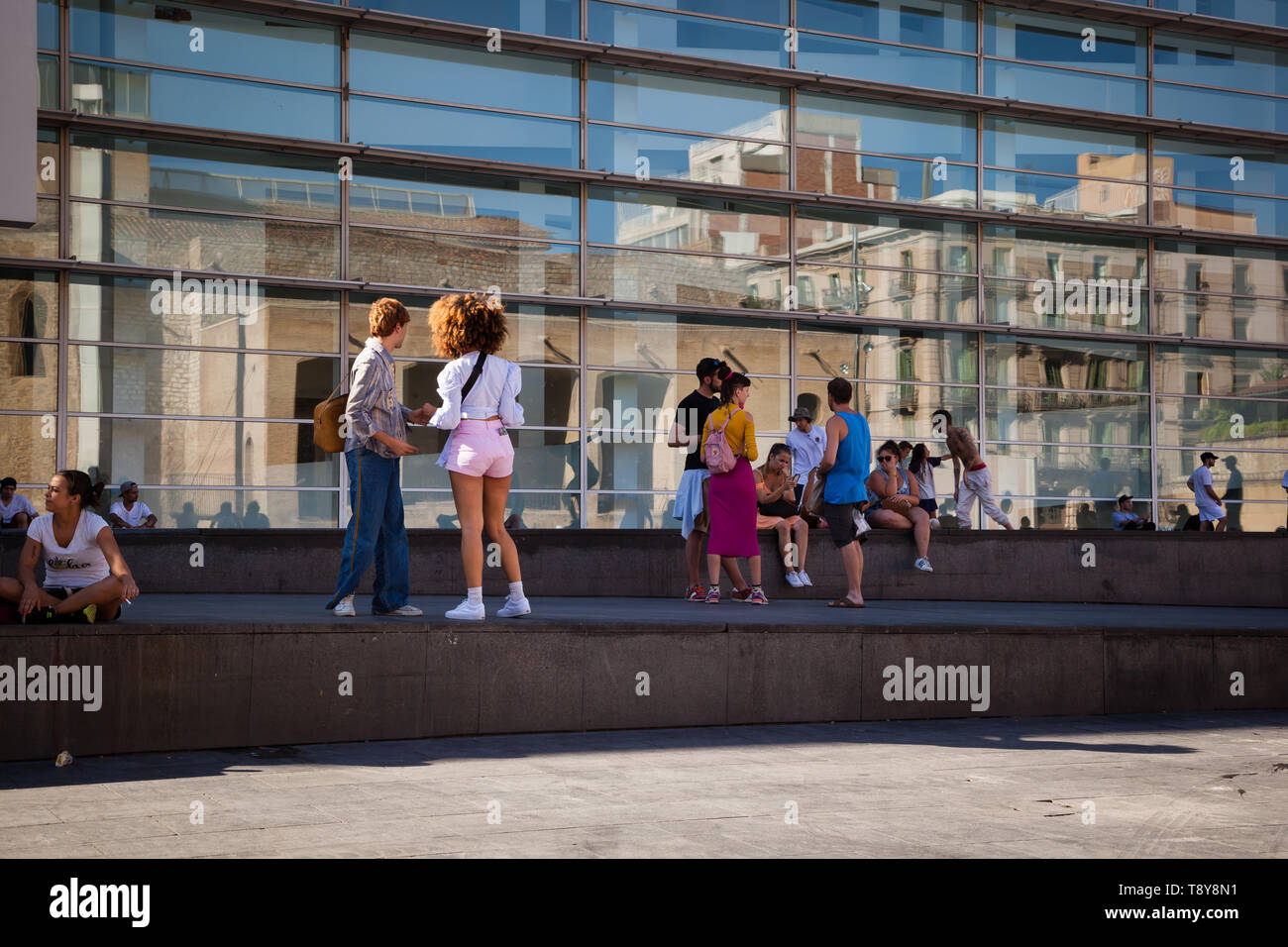 Young people in front of modern building with glass facade and reflections of old buildings, Barcelona city center Stock Photo