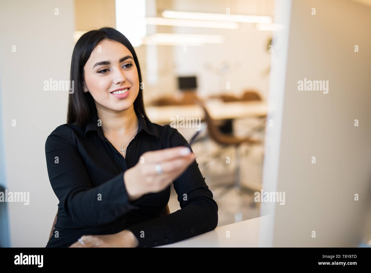 Smiling businesswoman pointing screen of pc with pen in her office ...