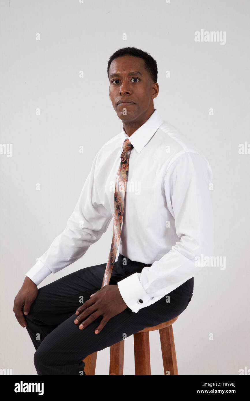 Black business man in white shirt and tie sitting on a wooden stool Stock Photo