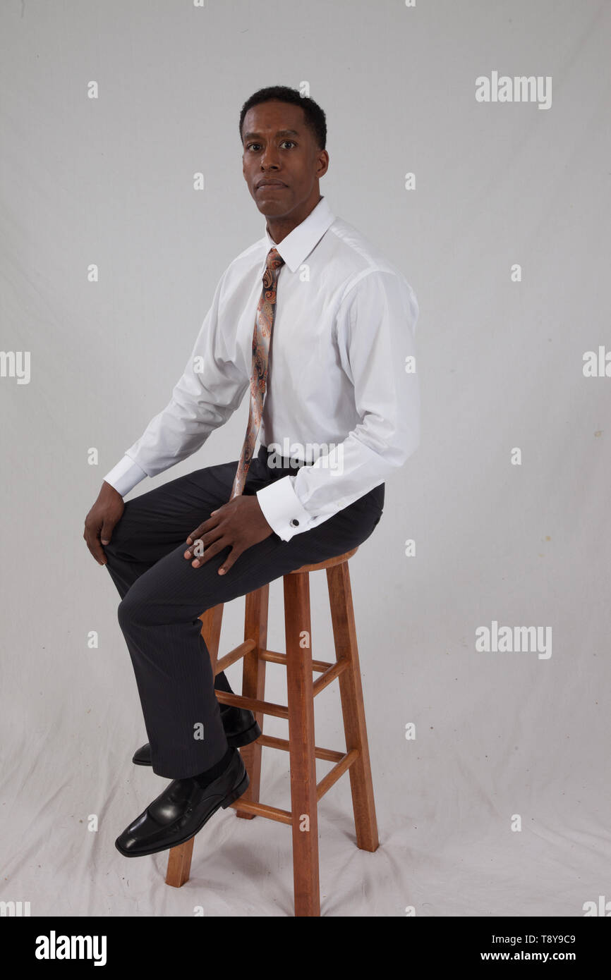 Black business man in white shirt and tie sitting on a wooden stool Stock Photo